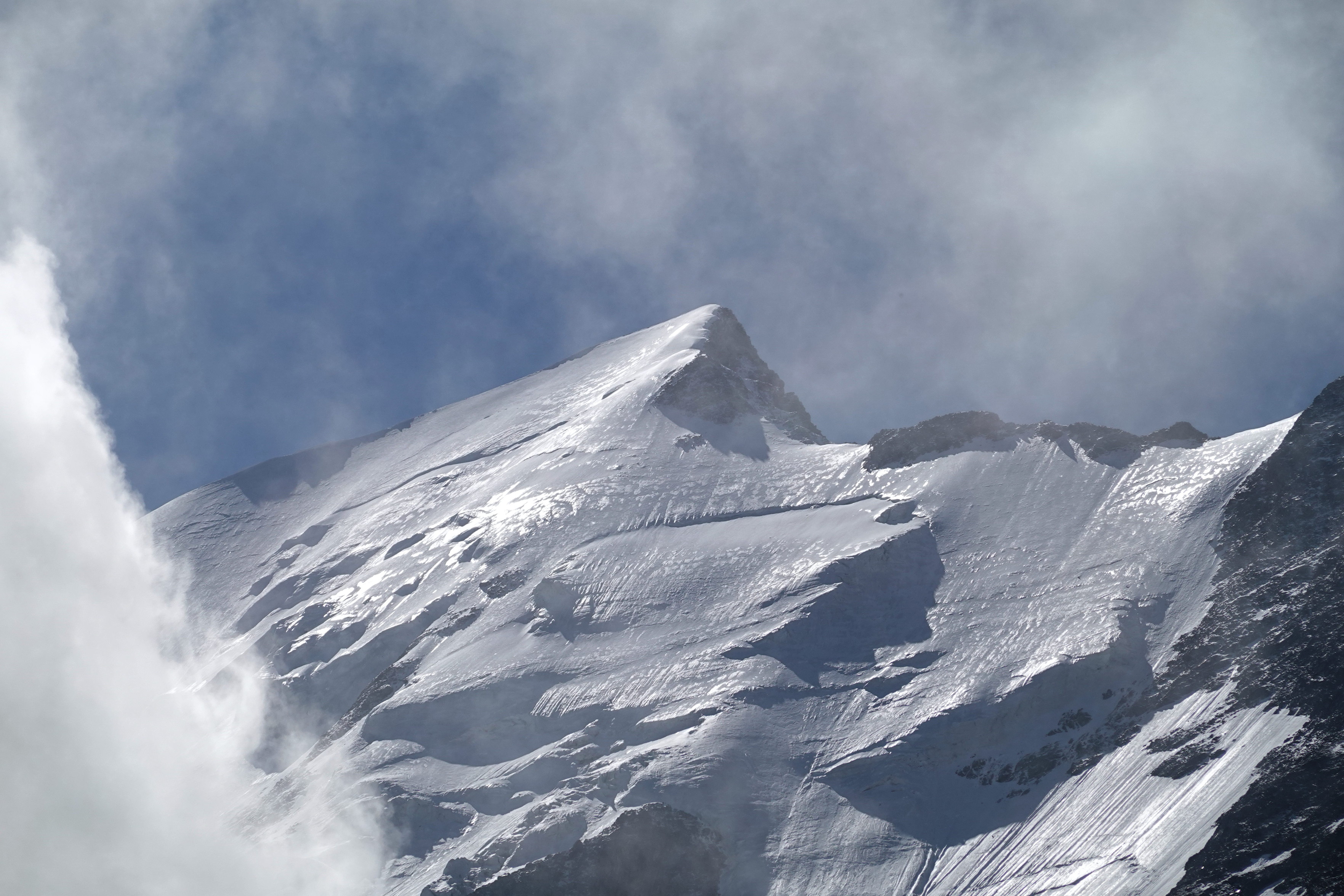 Snow-covered peak under a blue sky with some clouds, and a big cloud to the left.