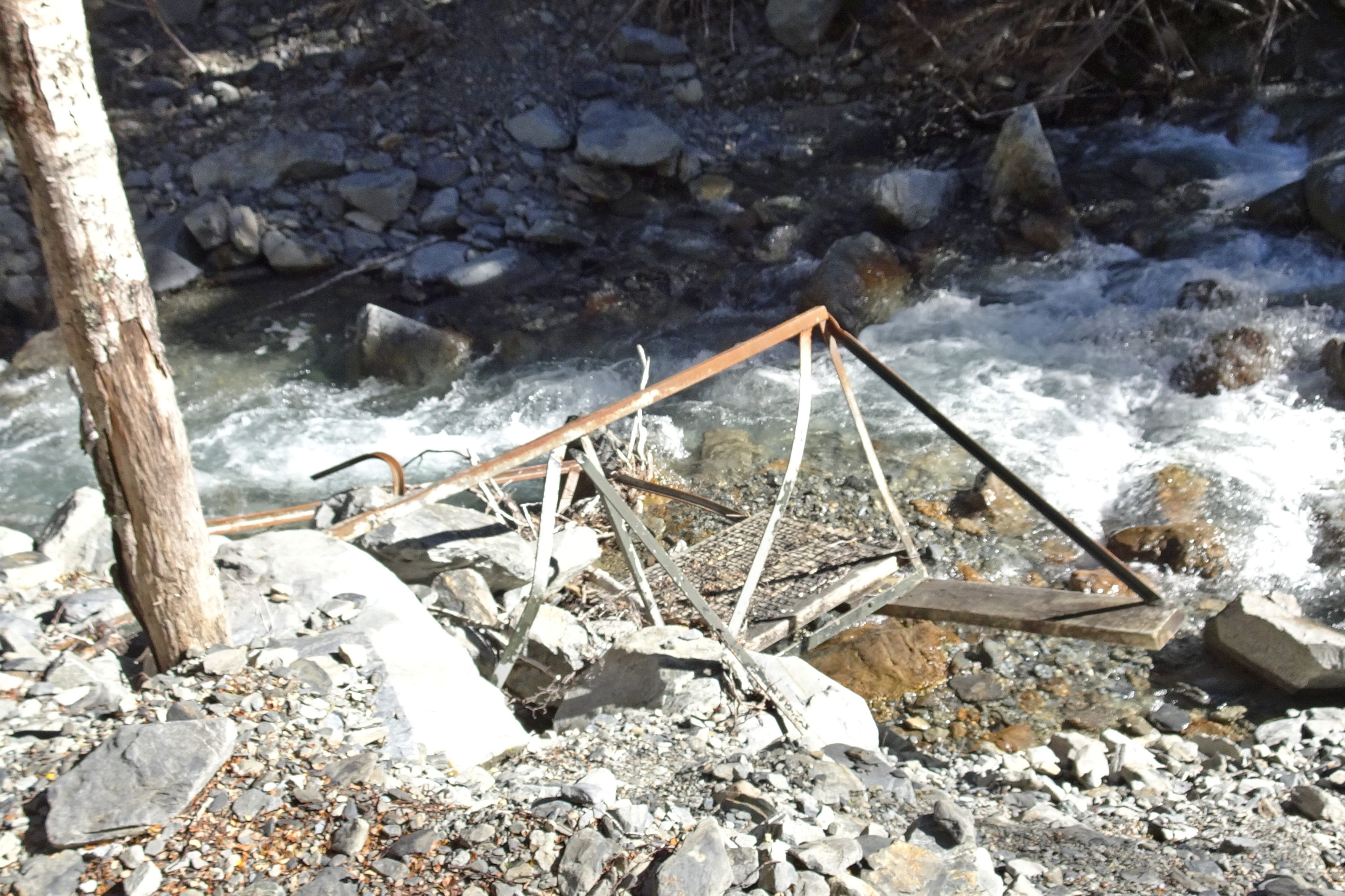 Broken bridge parts on the banks of a stream which has rapids here.