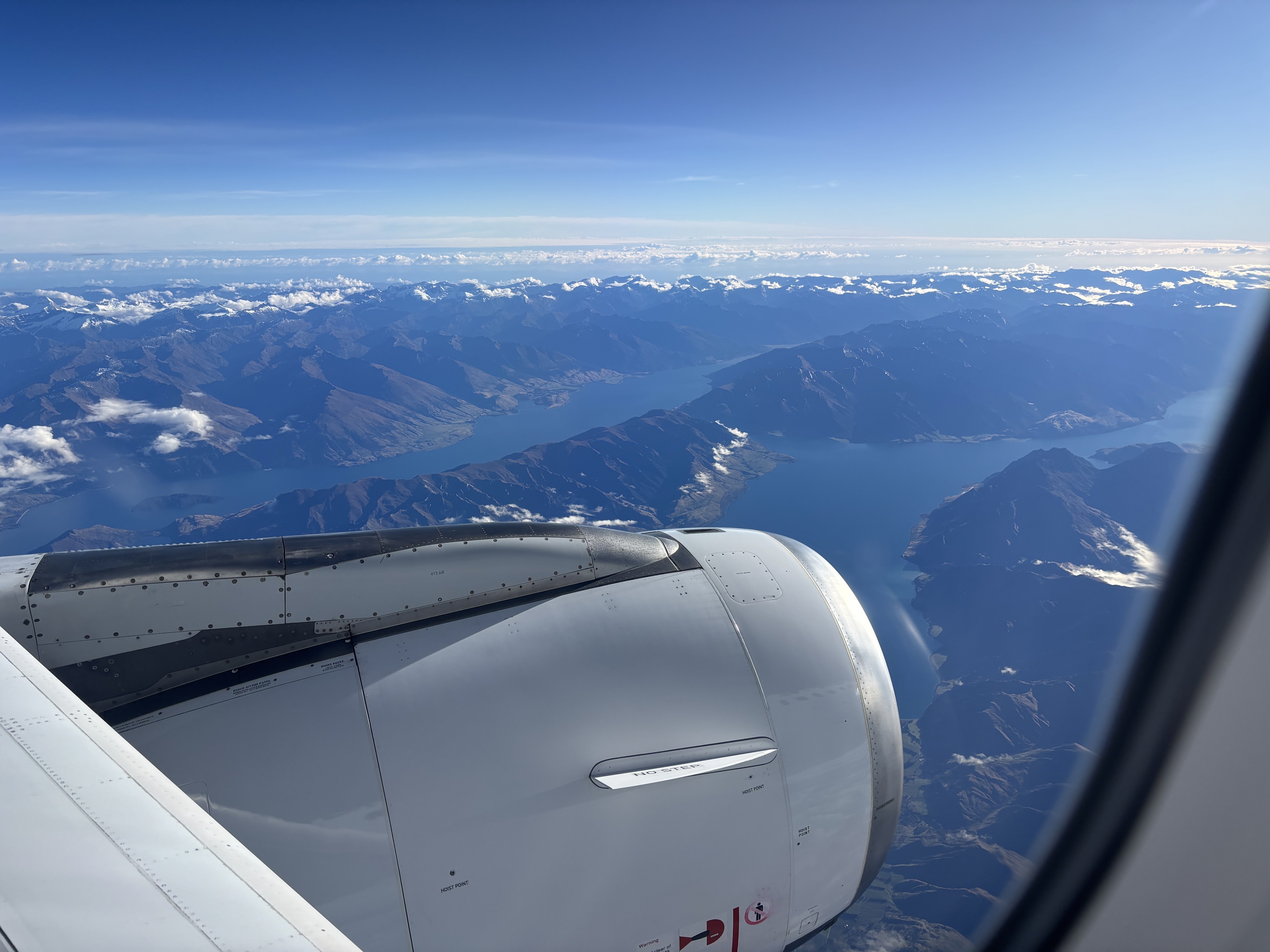 The view out the window from seat 10A in an Air New Zealand Airbus A320 airliner - blue skies, a deep blue lake in a mountainous valley.