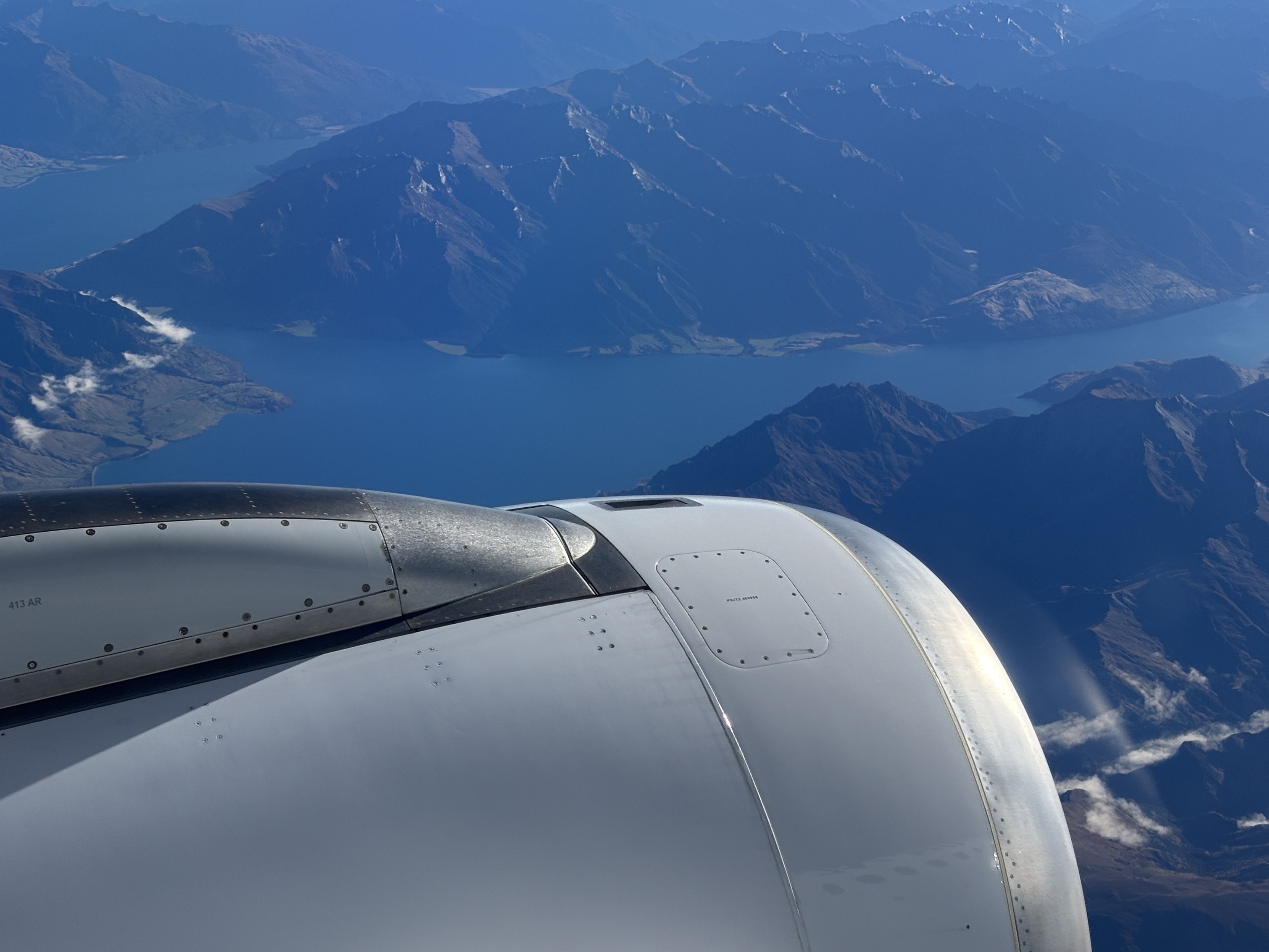 The view out the window from seat 10A in an Air New Zealand Airbus A320 airliner - blue skies, a deep blue lake in a mountainous valley.