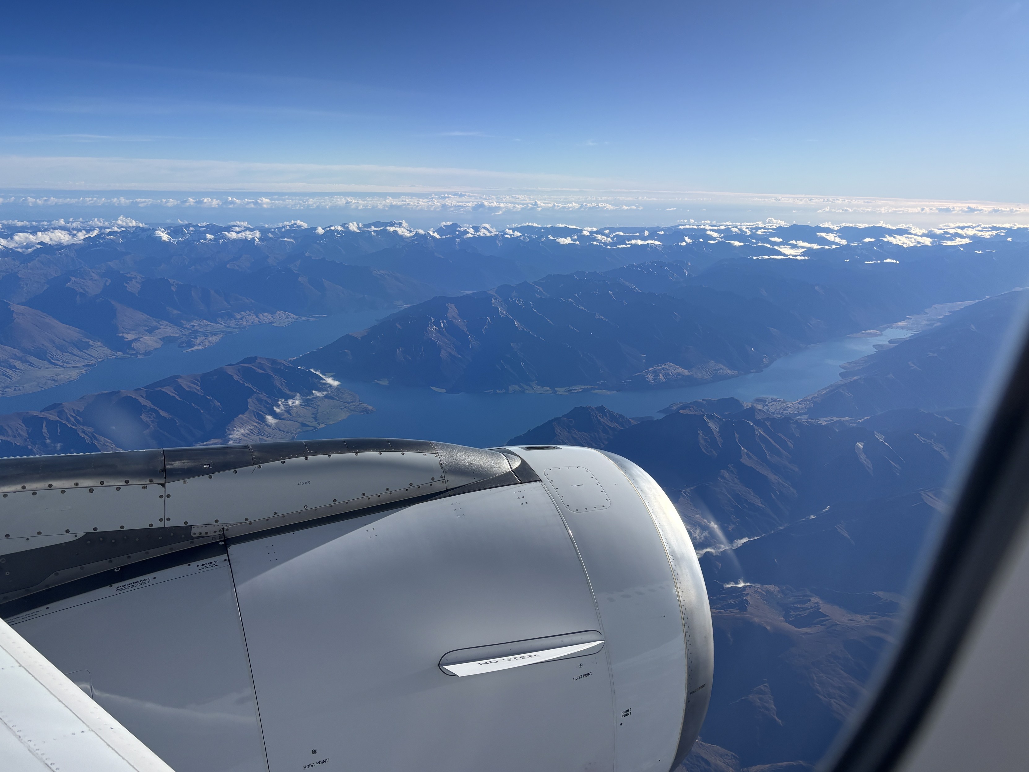 The view out the window from seat 10A in an Air New Zealand Airbus A320 airliner - blue skies, a deep blue lake in a mountainous valley.