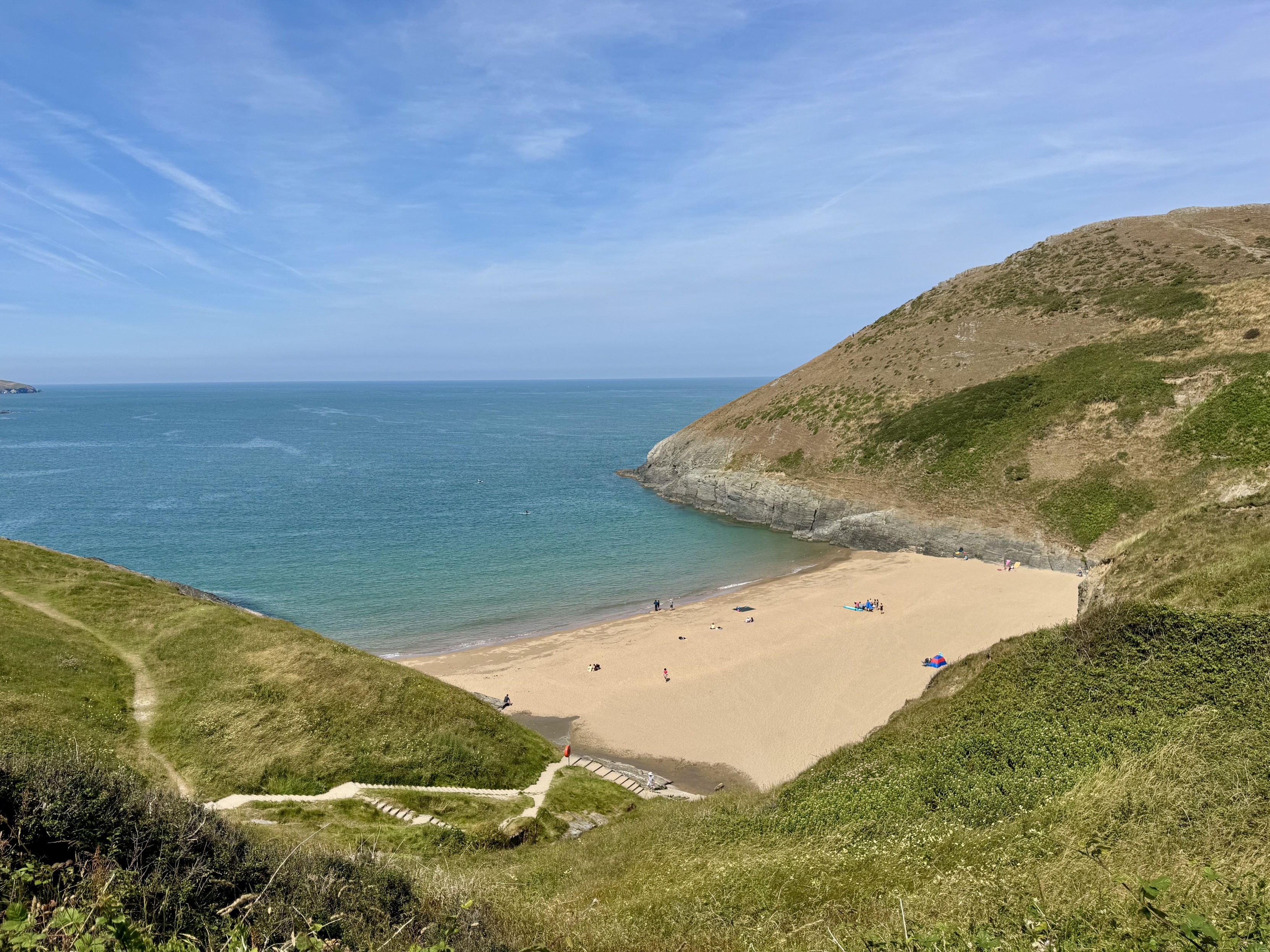 Small sandy beach at the bottom of scrub-covered hills; steps descend to it left of frame