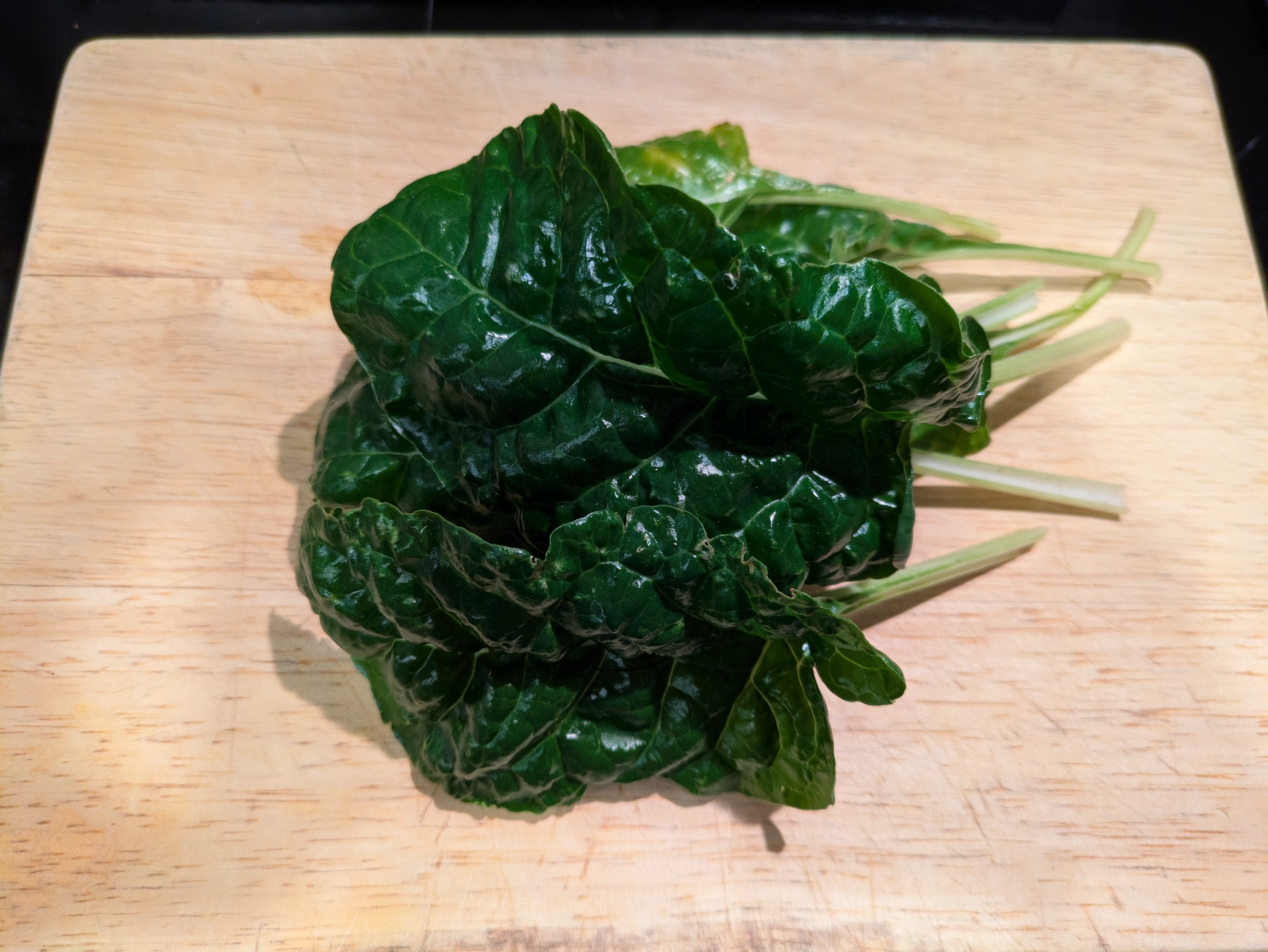 A heap of silverbeet leaves on a wooden chopping board.